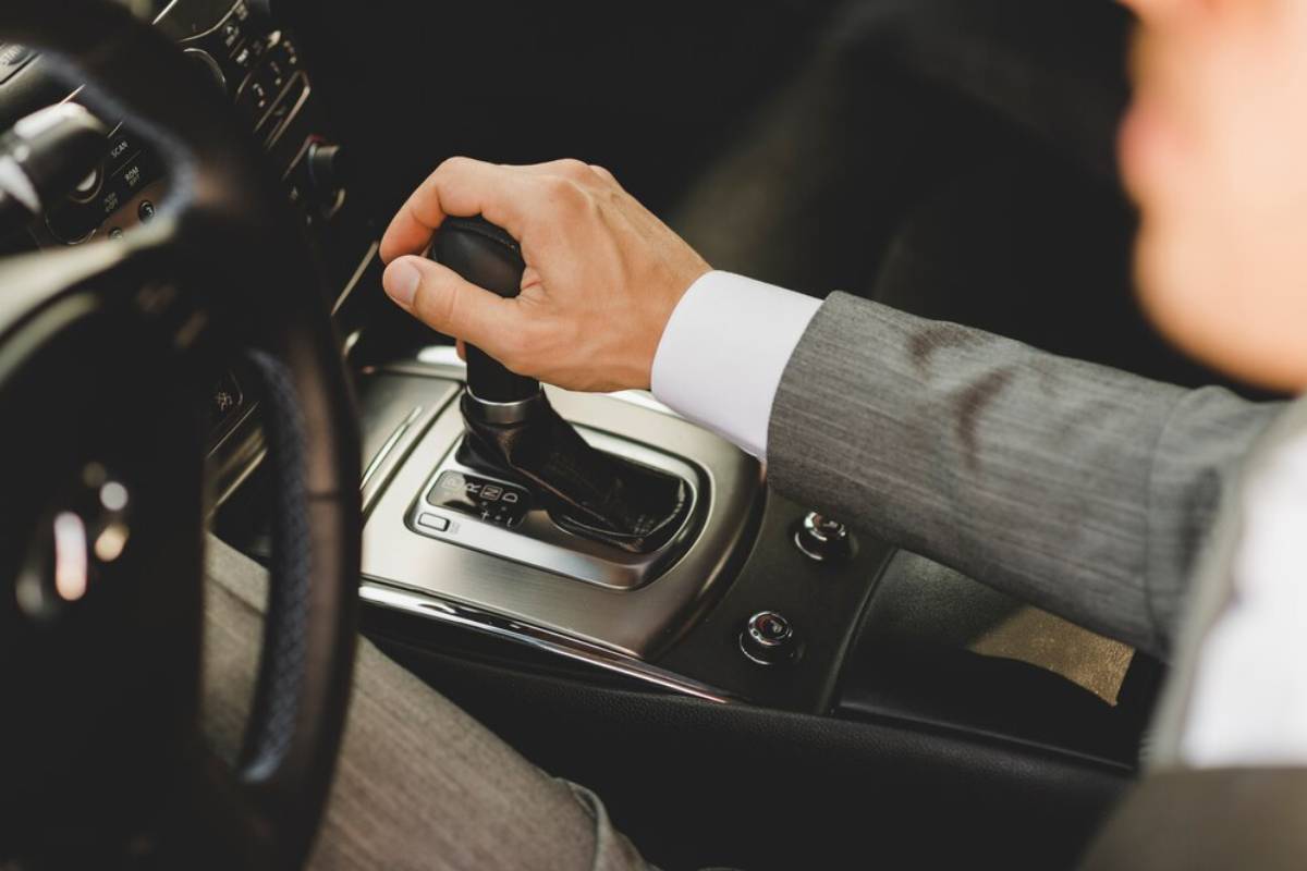 A close-up of a man's hand in a suit shifting gears in a luxury car's automatic gear lever.