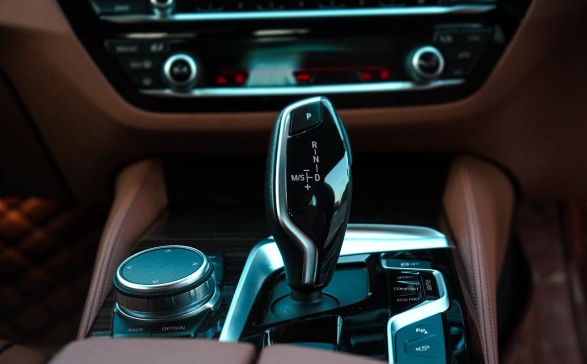 Close-up of a sleek car gear shifter with marked positions P, R, N, D, and S, beside a control dial, set in a luxurious interior.