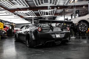 A sleek black Ferrari with a prominent rear wing is parked in a high-tech garage, surrounded by tools and other cars.