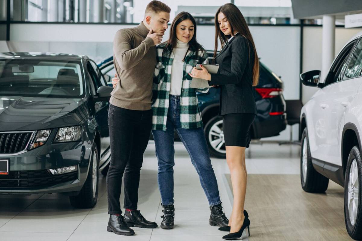 A couple engages with a female car salesperson in a modern car dealership, surrounded by various vehicles.