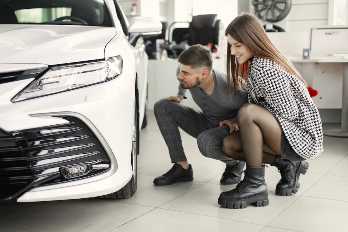 A young couple closely examines a sleek white car in a modern dealership.