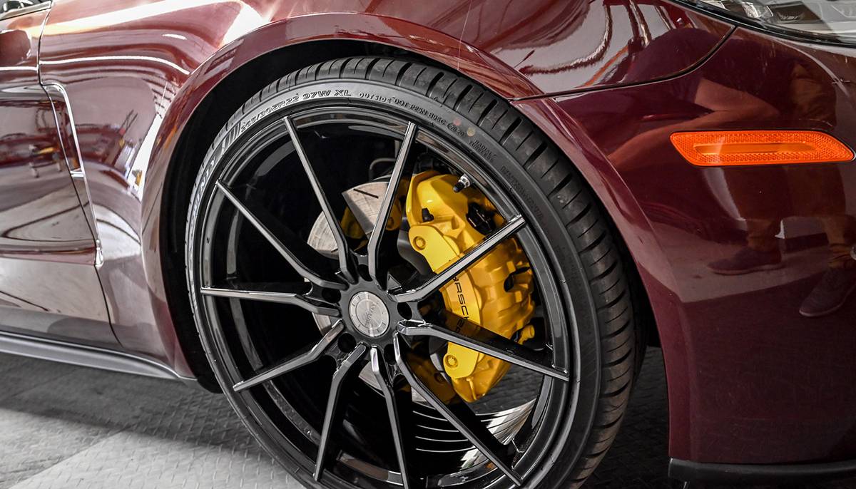 Close-up of a sleek maroon sports car’s wheel showcasing a black alloy rim and bright yellow brake calipers.