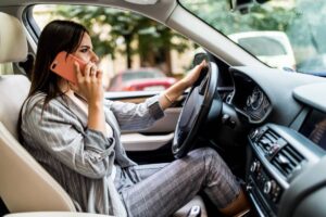 A woman sitting in a car, wearing a striped outfit, holding a phone to her ear while driving.