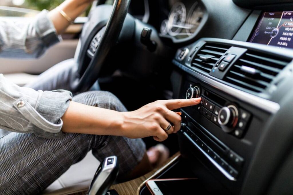A person in a car adjusts the radio settings, focusing on the dashboard controls while holding the steering wheel.