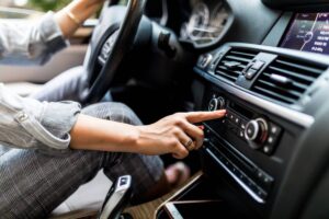 A person in a car adjusts the radio settings, focusing on the dashboard controls while holding the steering wheel.