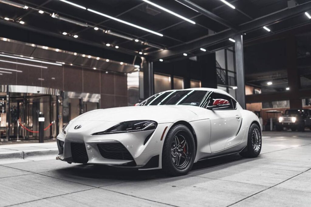 A sleek white Toyota Supra parked stylishly under modern lighting in an urban setting.