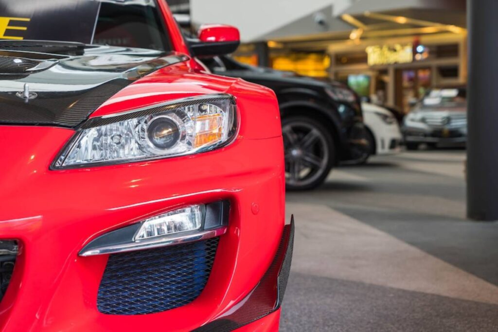 A close-up of a vibrant red sports car's front, featuring sleek headlights and a carbon fiber hood.