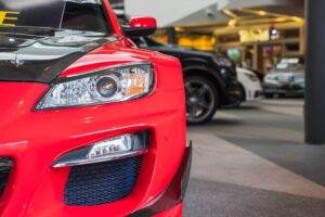 A close-up of a vibrant red sports car's front, featuring sleek headlights and a carbon fiber hood.