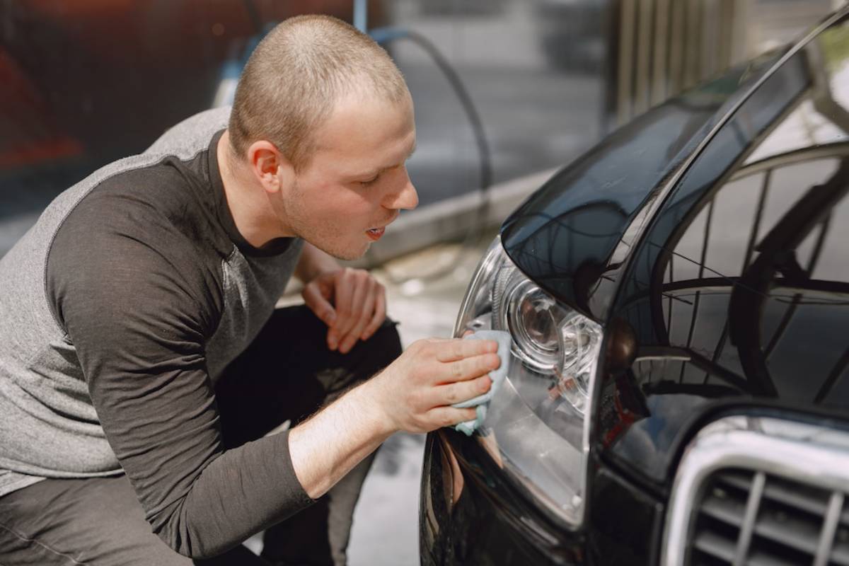 A person attentively cleans the headlight of a black car with a cloth, showcasing meticulous care and attention to detail.