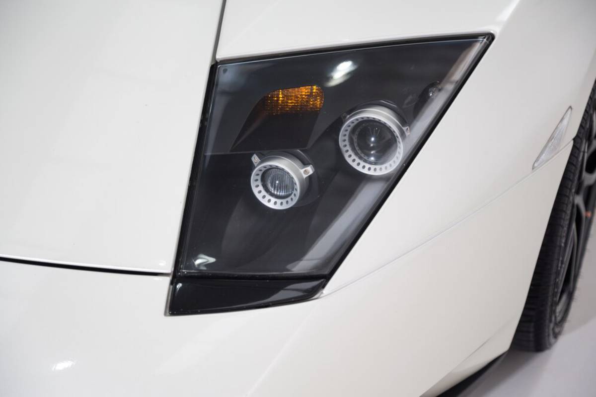 Close-up of a sleek white car's headlight, showcasing modern design with circular LED accents and a stylish dark lens.