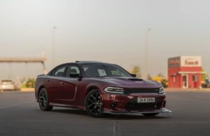 A sleek maroon Dodge Charger parked at an empty lot, showcasing its sporty design and distinctive black alloy wheels.