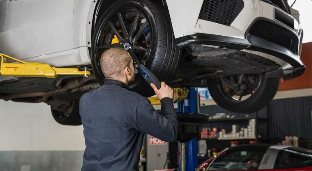 A mechanic working under a raised car, using a power tool to adjust the tire.