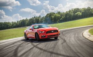 A vibrant red sports car drifts on a racetrack, leaving tire marks, with lush green fields.