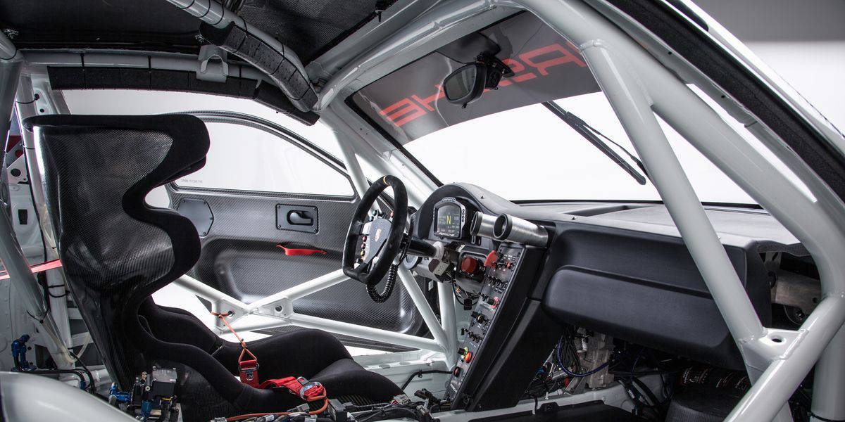Interior of a race car featuring a carbon fiber seat, racing steering wheel, and a dashboard with various controls and gauges.