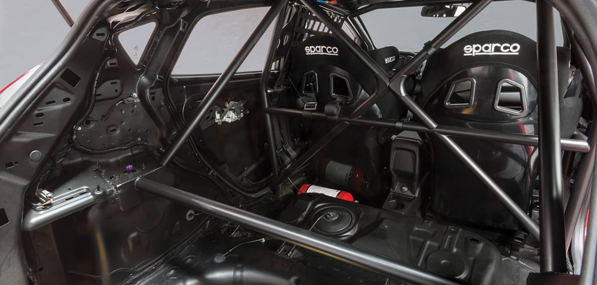 Interior of a race car featuring two Sparco racing seats and a robust roll cage for enhanced safety and structural integrity.