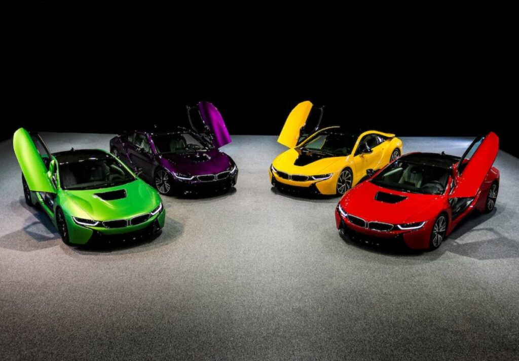 Four BMW i8 sports cars in vibrant colors—green, purple, yellow, and red—displayed with doors open against a dark background.