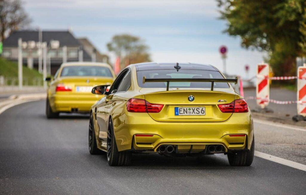 A vibrant yellow BMW M4 coupe drives ahead of a matching BMW sedan, showcasing sleek designs against a road backdrop.