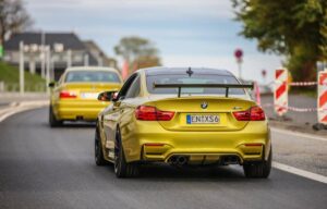 A vibrant yellow BMW M4 coupe drives ahead of a matching BMW sedan, showcasing sleek designs against a road backdrop.