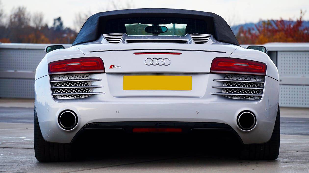 A rear view of a white Audi R8 convertible, showcasing its sleek design, distinctive taillights, and dual exhaust.
