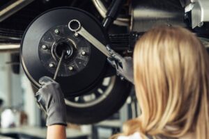 A mechanic with blonde hair repairs a car's brake system, using a wrench on the wheel hub.