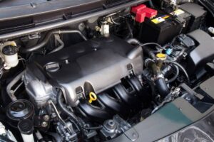 A detailed view of a car engine compartment showing various components like the battery, hoses, and fluid reservoirs.