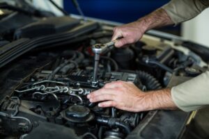 A mechanic uses a socket wrench on a car engine in a workshop.