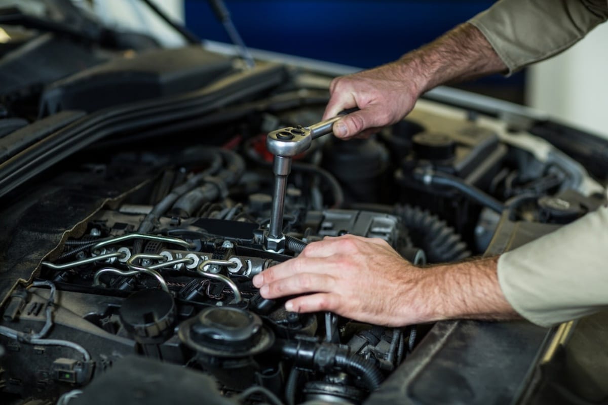A mechanic uses a socket wrench on a car engine in a workshop.