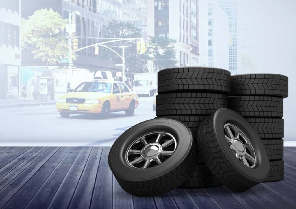 Piles of new car tyres in foreground with a blurred city street and taxi in the background.
