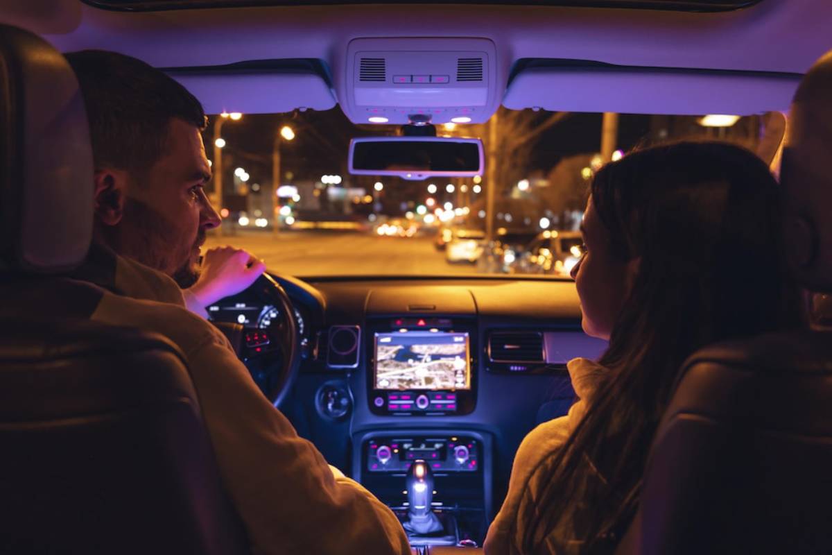 A man and a woman in a car at night, facing forward, with city lights visible outside.