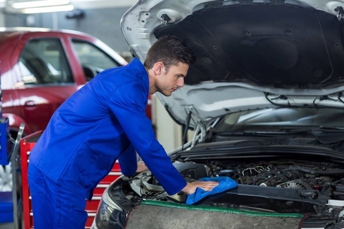  Mechanic in blue overalls inspecting a car engine in a workshop.