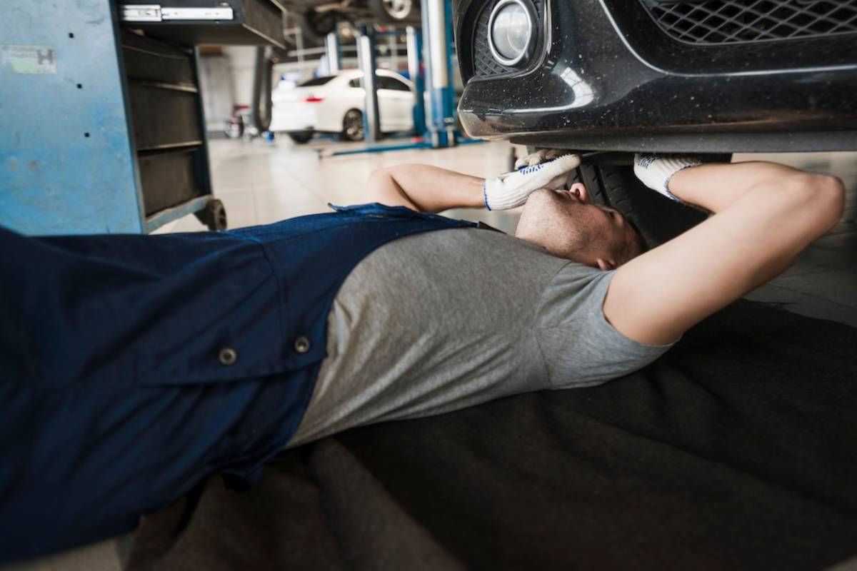 Mechanic lying on his back, working under a car in a garage.